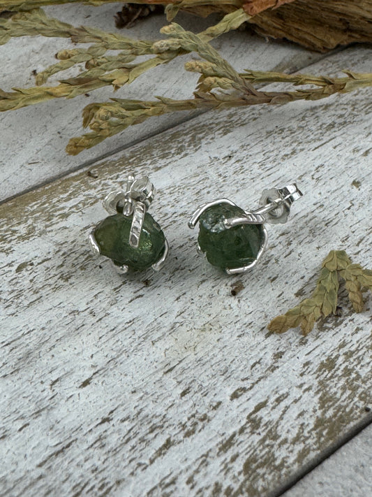 Green stone earrings on a rustic wooden surface with dried leaves.