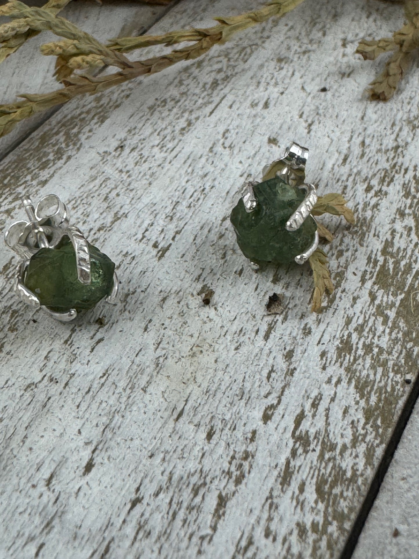 Green stone earrings with silver settings on a rustic wooden surface