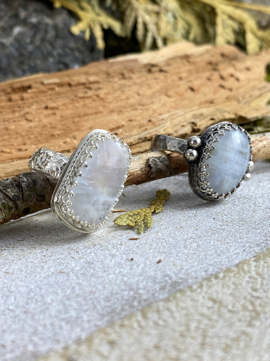 Two Rust and Leaf Sterling Silver Antique looking Moonstone Rings sitting on a white and natural wood background