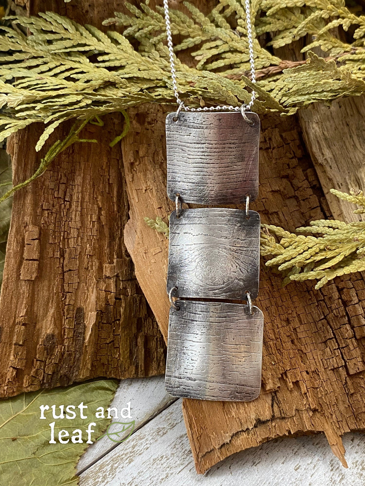 Rust and Leaf's Original Stitched Tree Bark Necklace made in Sterling Silver, featuring our signature Tree Bark texture, displayed against wood texture and branches