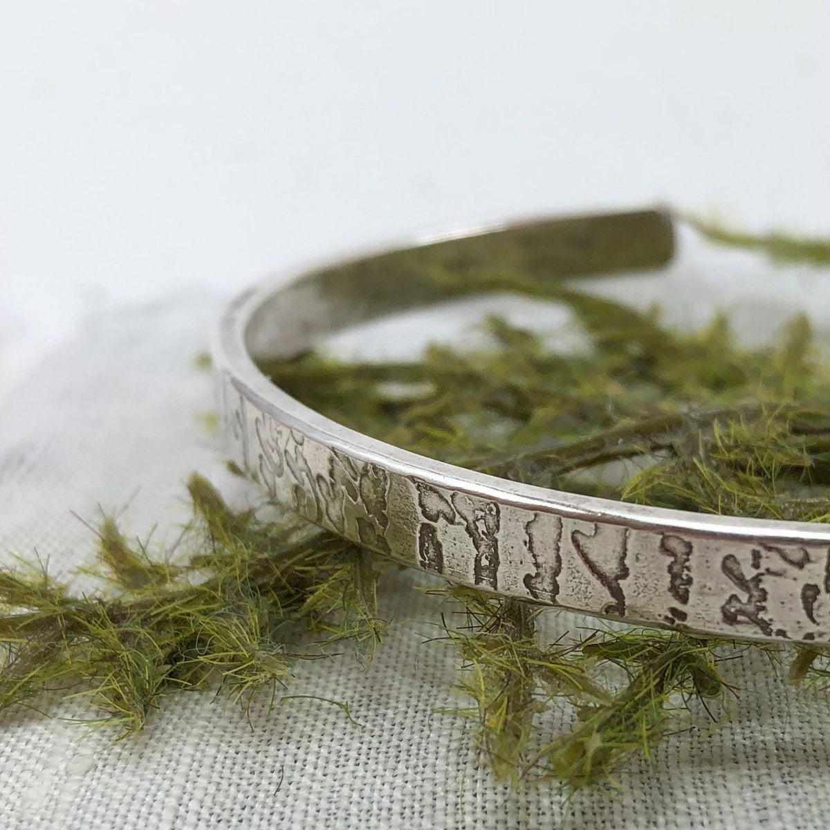 Sterling cuff with old handwriting etched in, sitting on a fern.