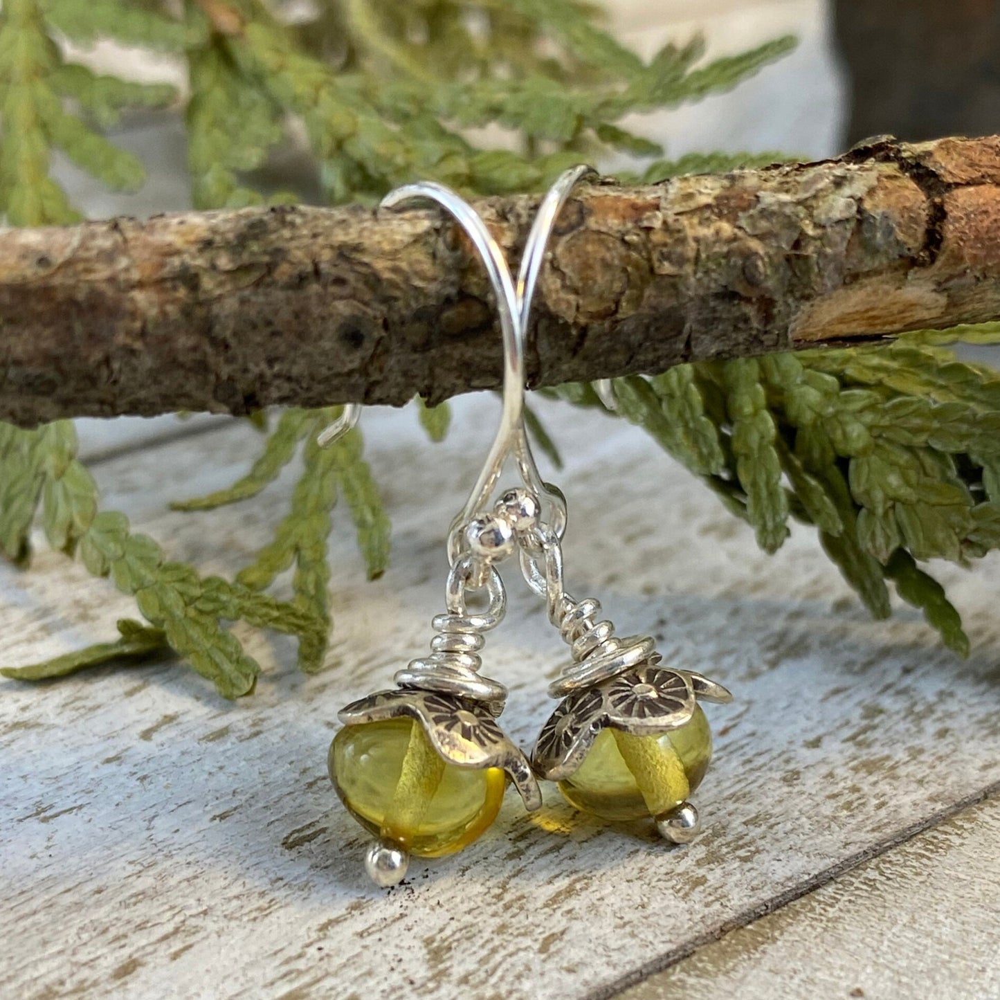 Sterling silver dangle earrings with baltic amber resting on a tree branch