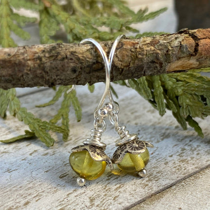 Sterling silver dangle earrings with baltic amber resting on a tree branch