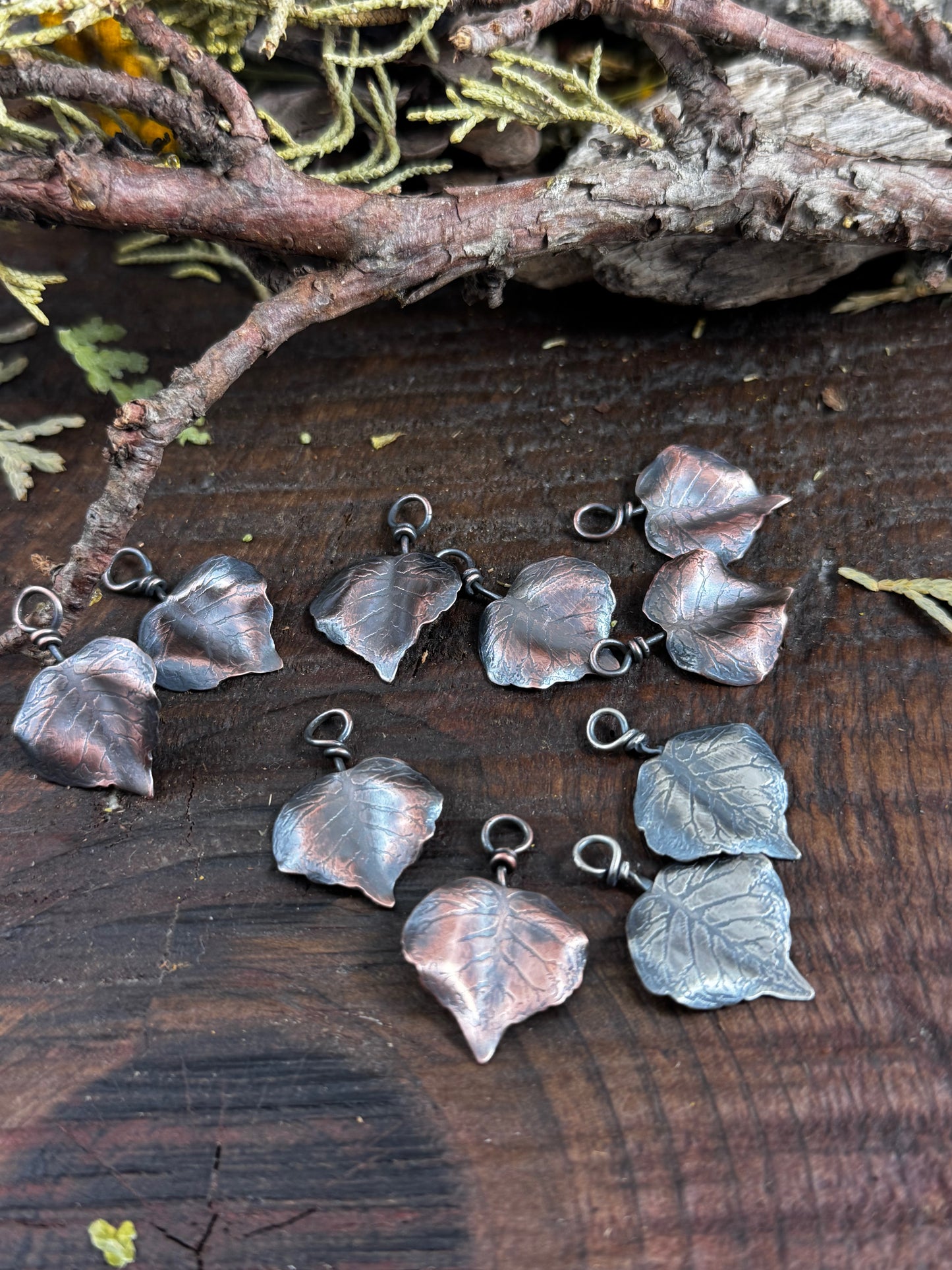 Silver and copper leaf-shaped charms on a wooden surface with natural elements.