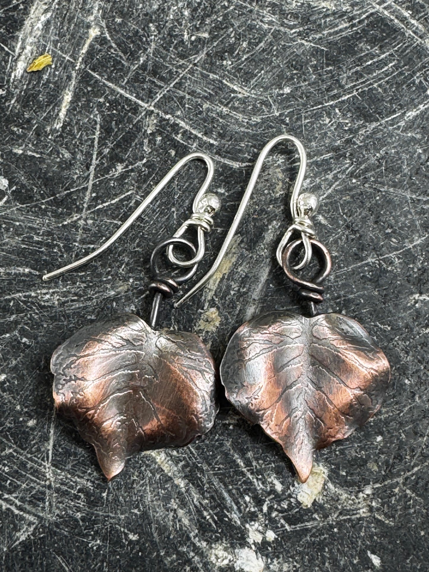 Copper leaf earrings on a textured dark surface