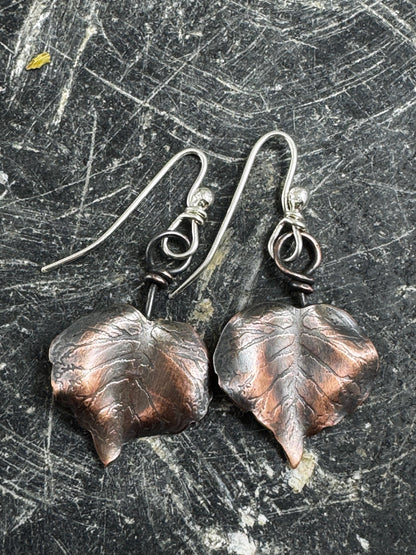 Copper leaf earrings on a textured dark surface