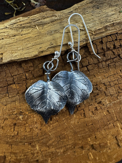 Silver leaf-shaped earrings on a wooden surface