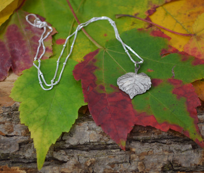 Birch Heart Leaf Necklace sitting on a colorful Maple Leaf and wood texture