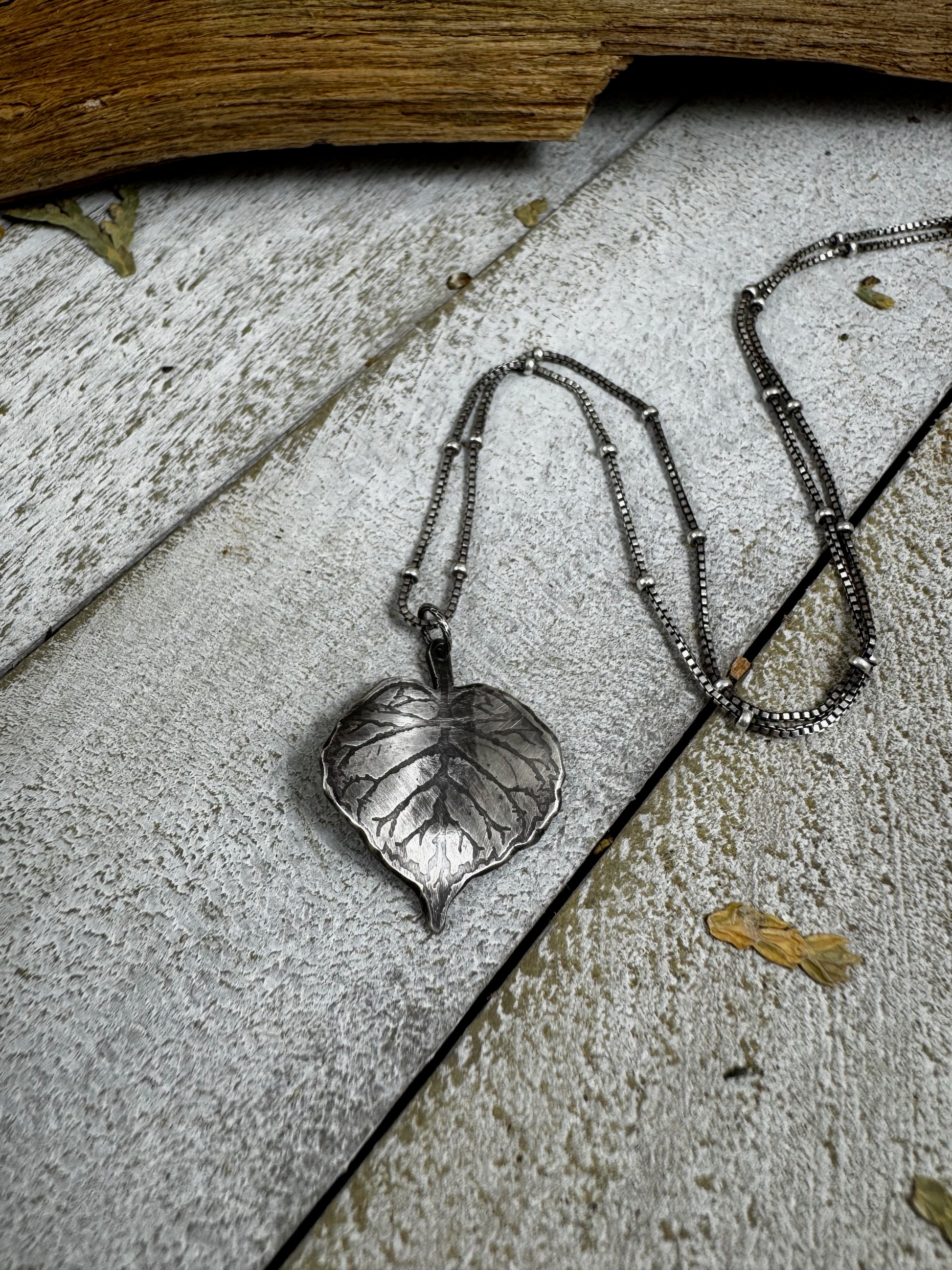 Silver leaf necklace on a weathered wood surface