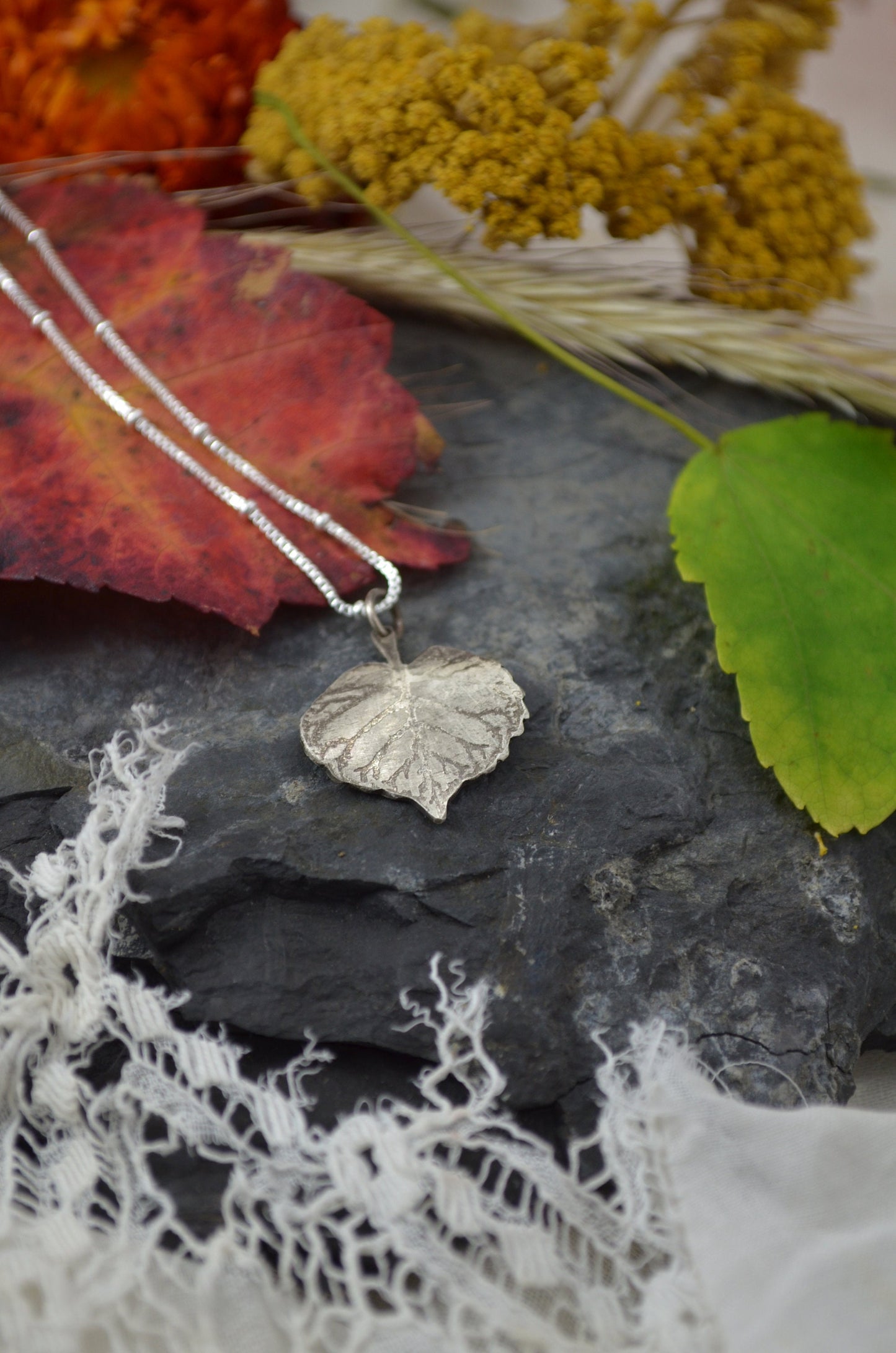 Birch Heart Leaf Necklace surrounded by colorful leaves and  natural textures