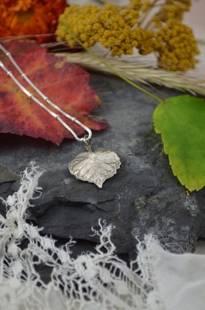 Birch Heart Leaf Necklace surrounded by colorful leaves and  natural textures