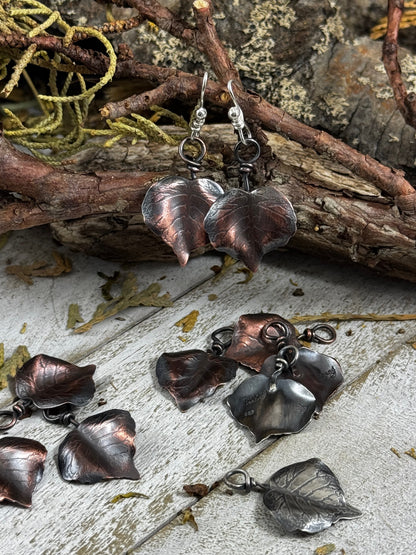 Copper leaf-shaped earrings on a natural background with twigs and leaves.