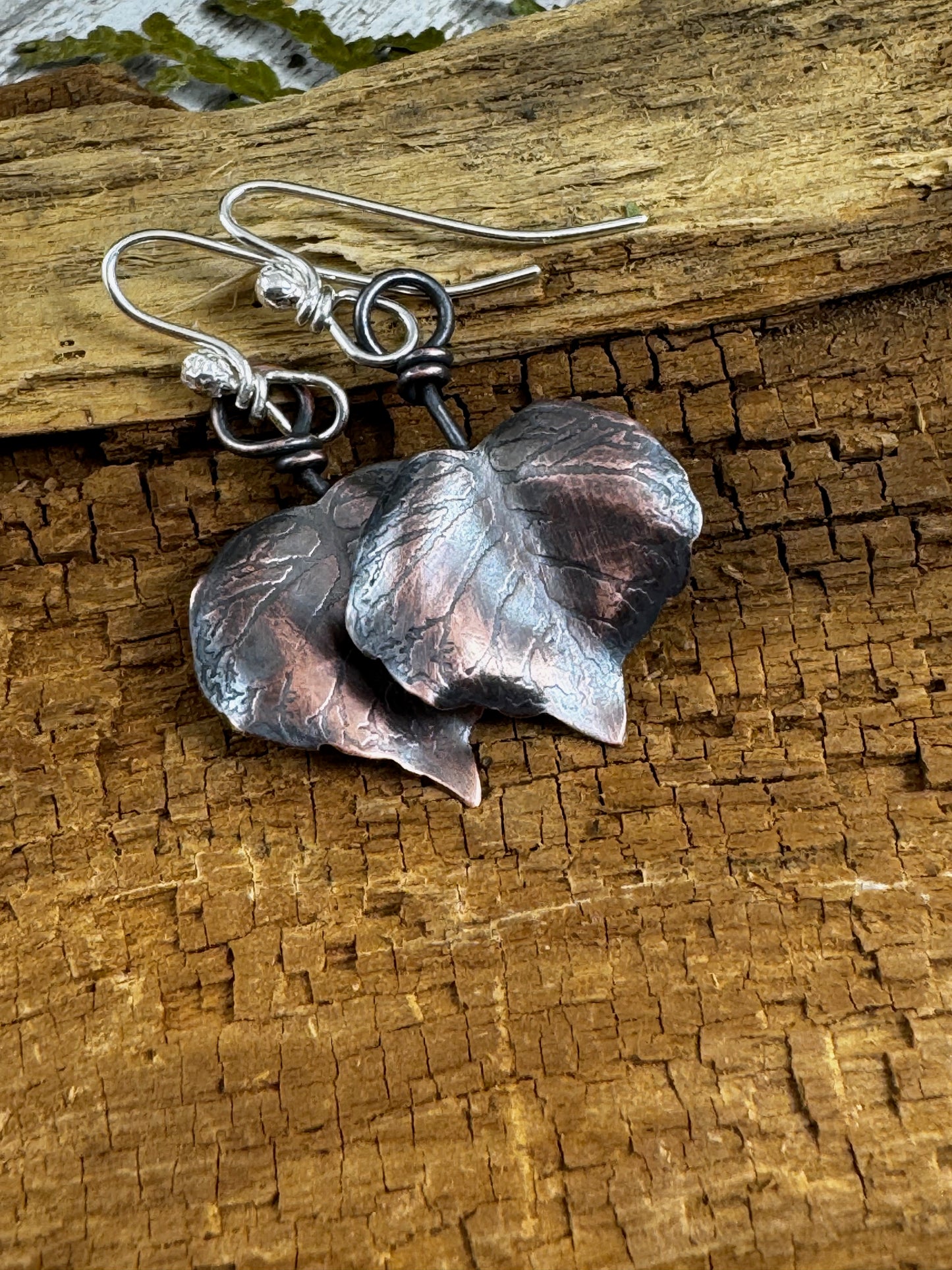 Copper heart shaped leaf earrings from Rust and Leaf on a wooden surface