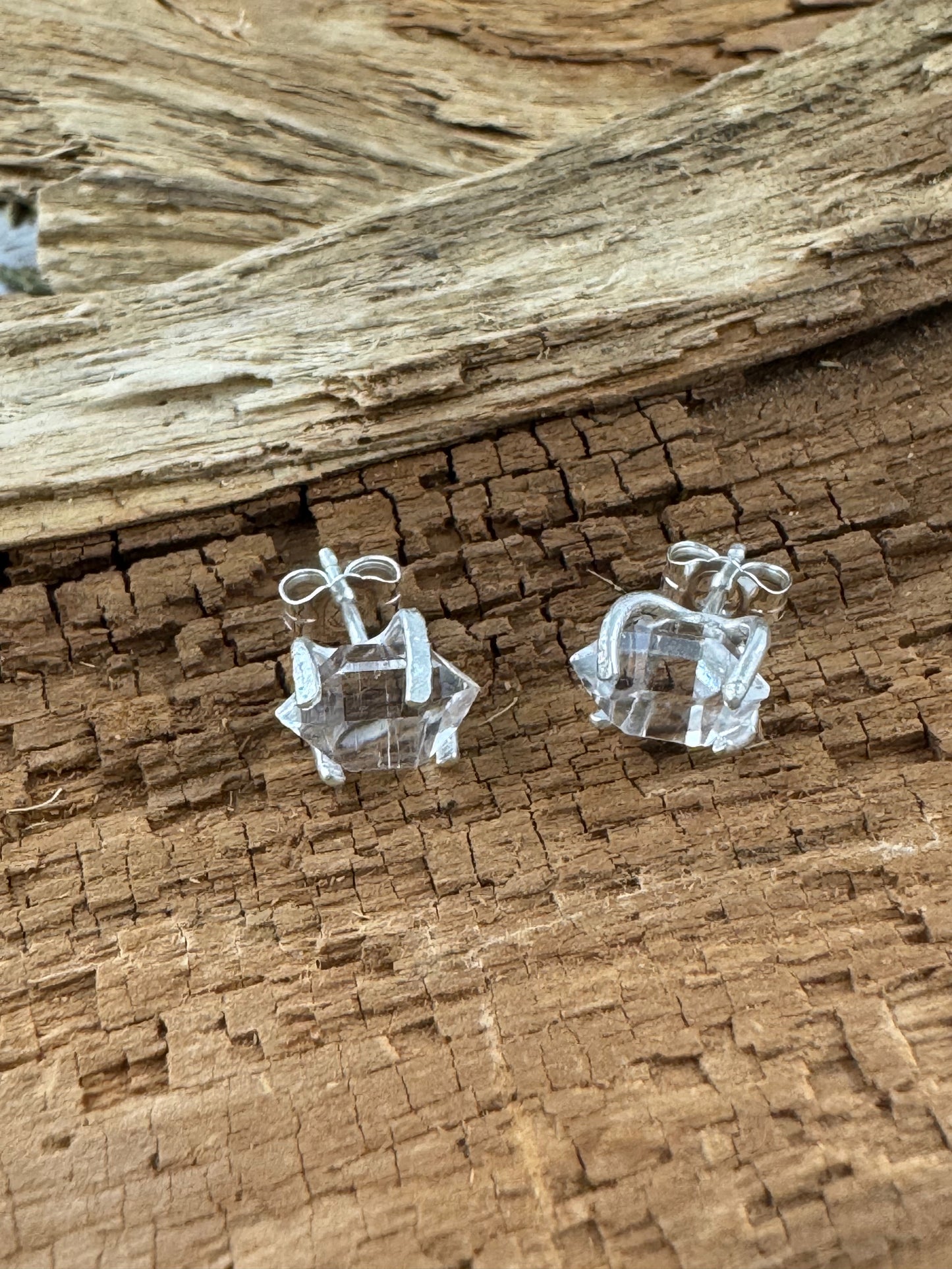 Sterling silver stud earrings with raw double-terminated Herkimer diamonds, handcrafted settings with optional tree bark texture, sitting on wood textured surface.