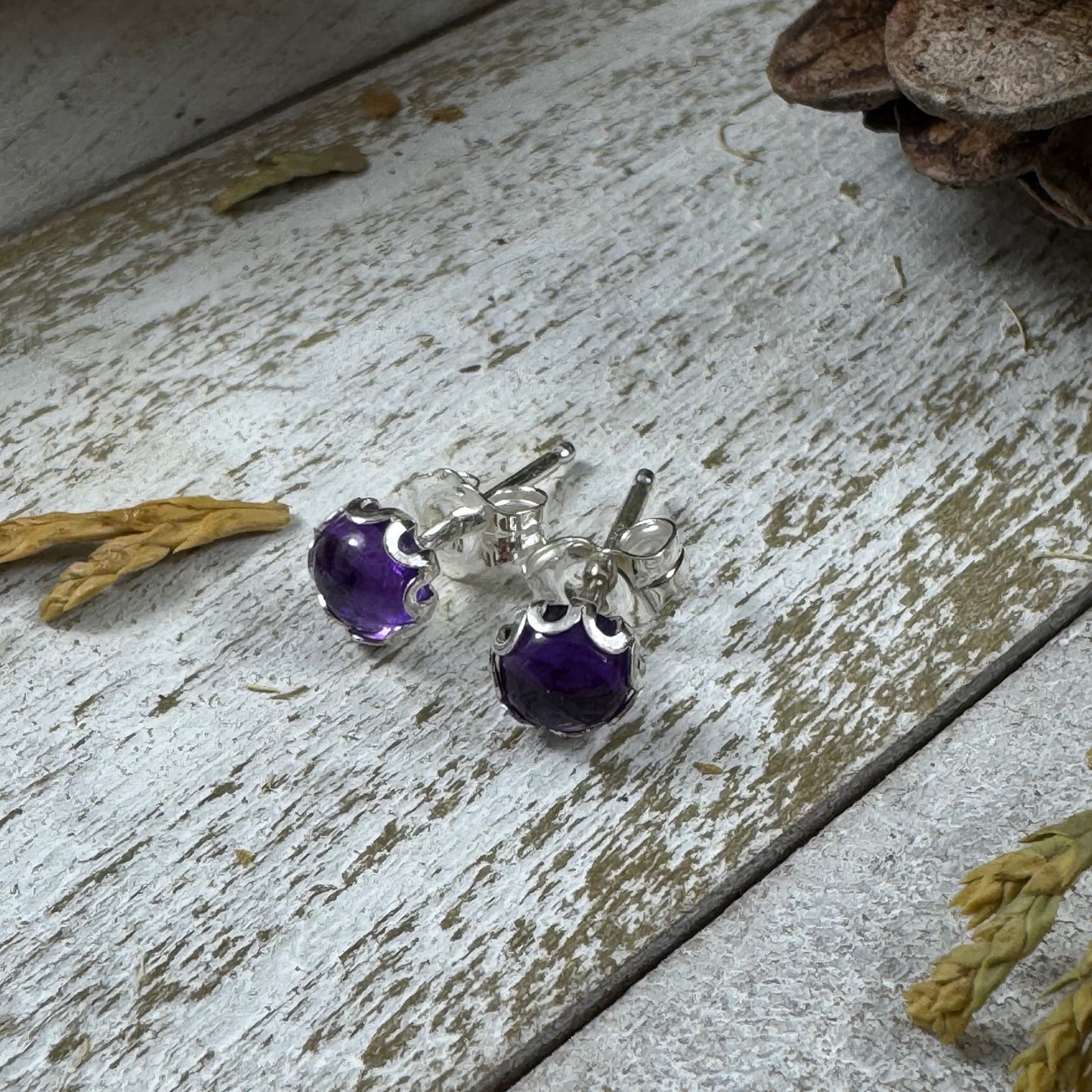 Sterling silver amethyst stud earrings with flower bezel on rustic wood background