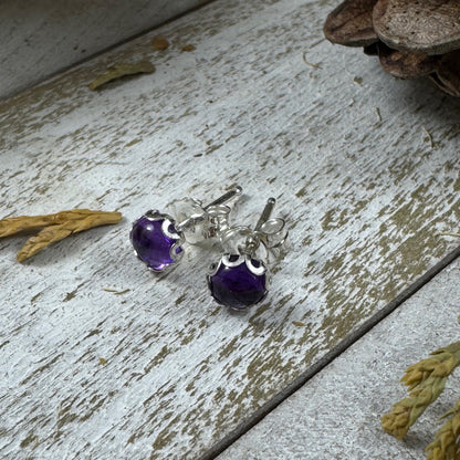Sterling silver amethyst stud earrings with flower bezel on rustic wood background