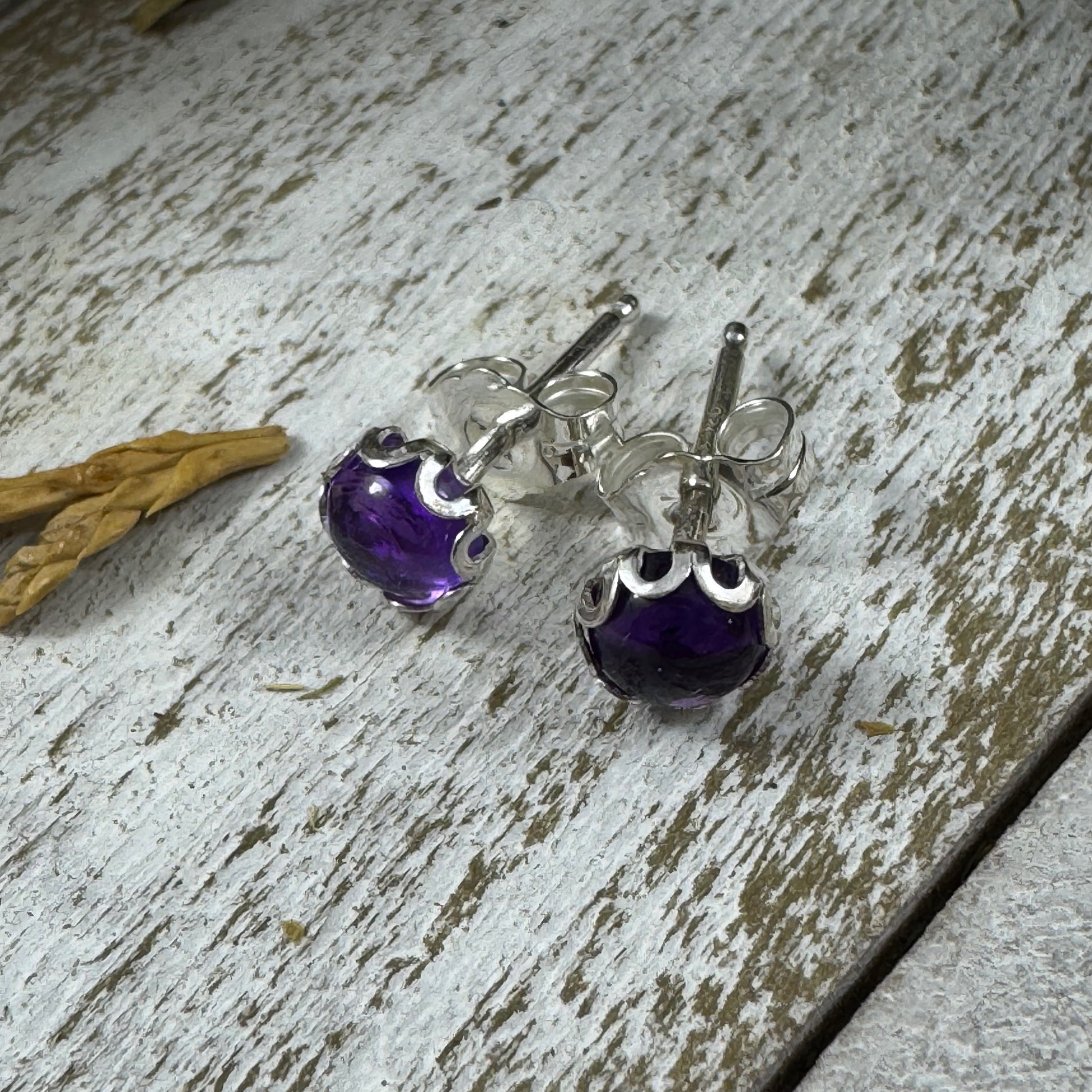Sterling silver amethyst stud earrings with flower bezel on rustic wood background