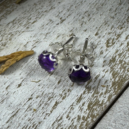 Sterling silver amethyst stud earrings with flower bezel on rustic wood background