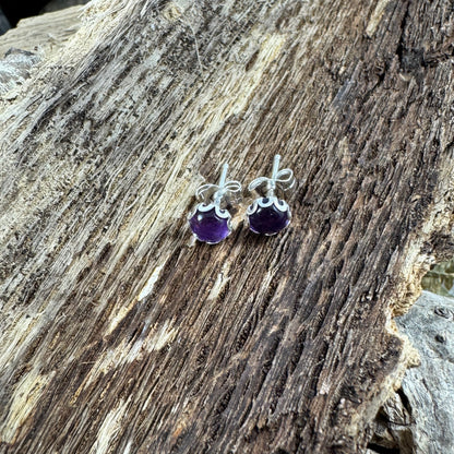 Sterling silver amethyst stud earrings with flower bezel on rustic wood background