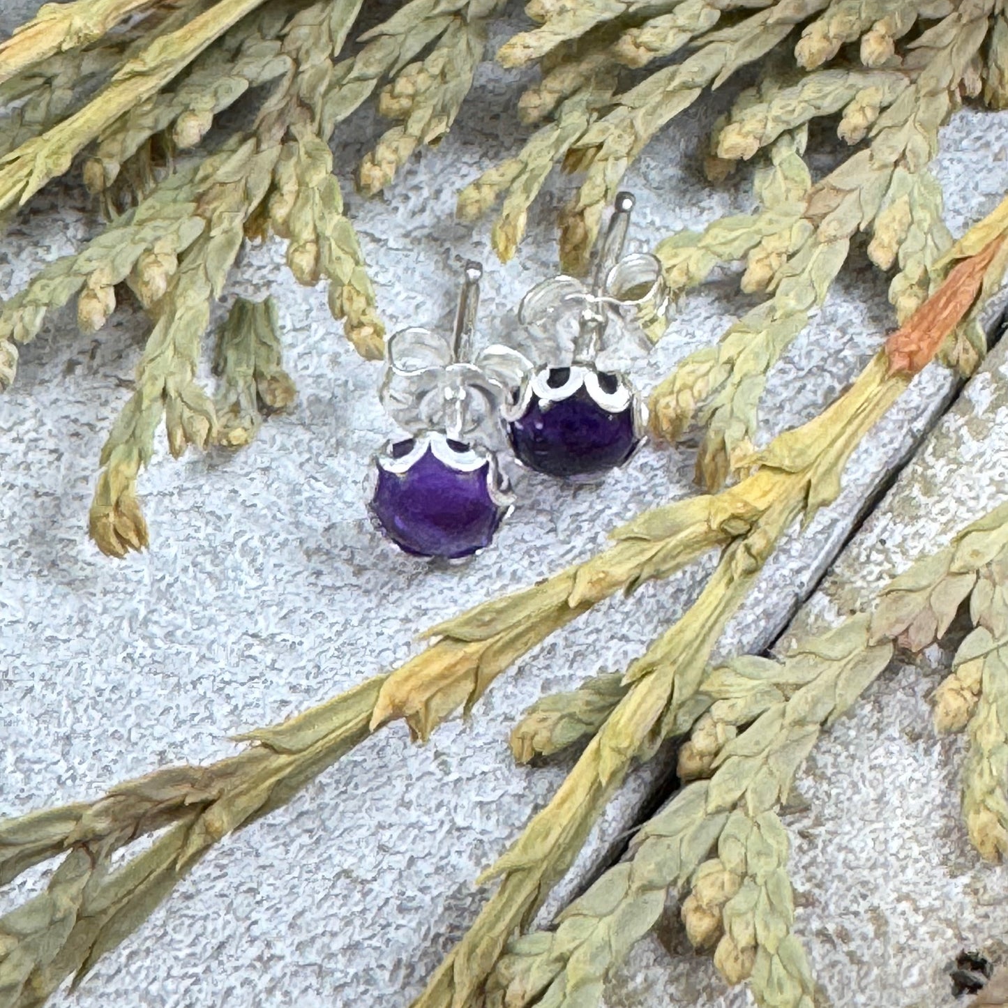 Sterling silver amethyst stud earrings with flower bezel on rustic wood background and plants
