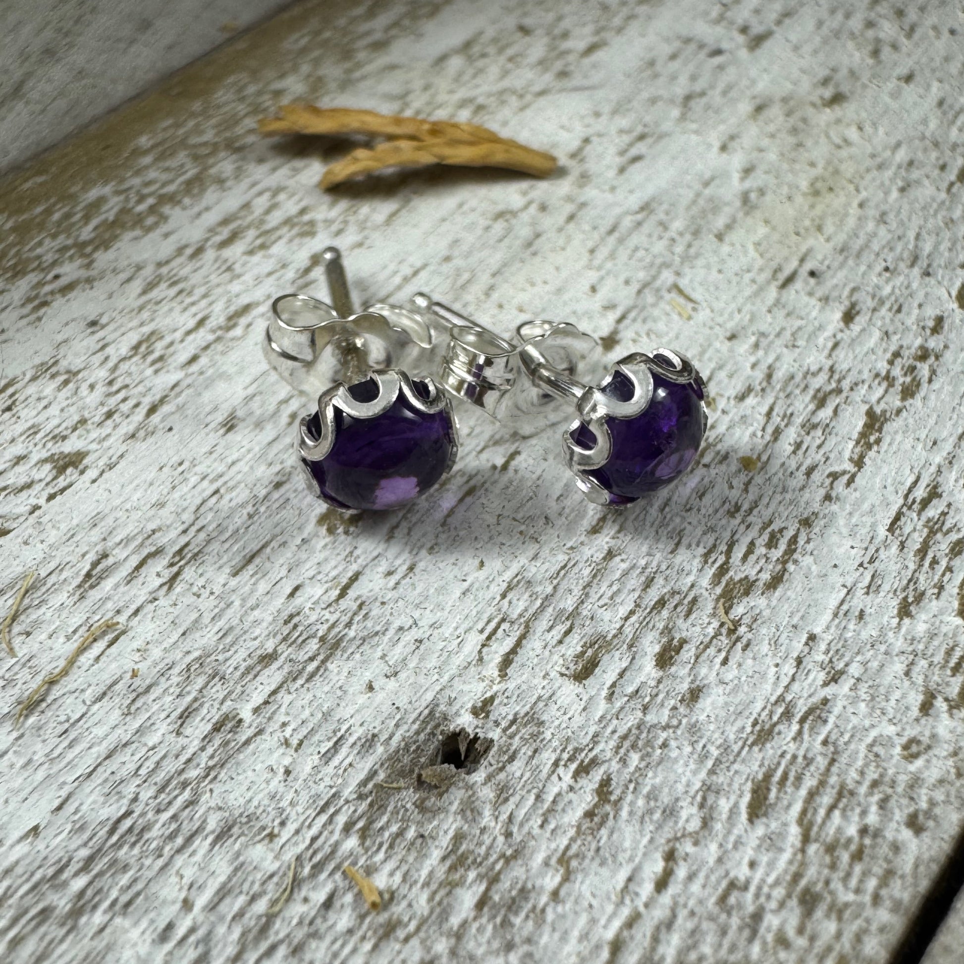 Sterling silver amethyst stud earrings with flower bezel on rustic wood background