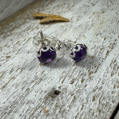 Sterling silver amethyst stud earrings with flower bezel on rustic wood background