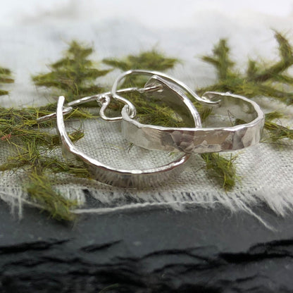 Sterling Silver Minimalist Hammered Hoops by Rust and Leaf laying on a multiple textured surface