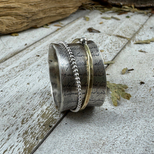 Sterling silver spinner ring with a brass band and silver ball detail, featuring partial handwritten text from a historic 1739 Port wine shipping contract.