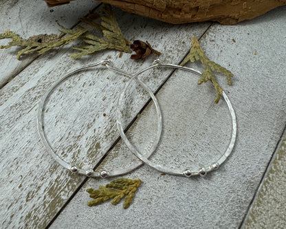 Medium Sterling Silver Hammered hoops next to leaves with three silver ball accents on each by Rust and Leaf