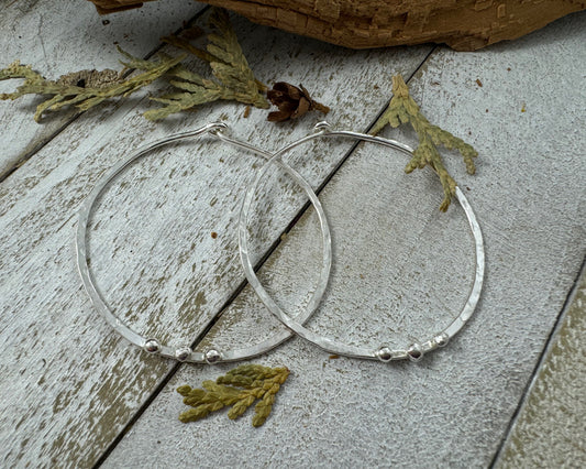 Medium Sterling Silver Hammered hoops next to leaves with three silver ball accents on each by Rust and Leaf