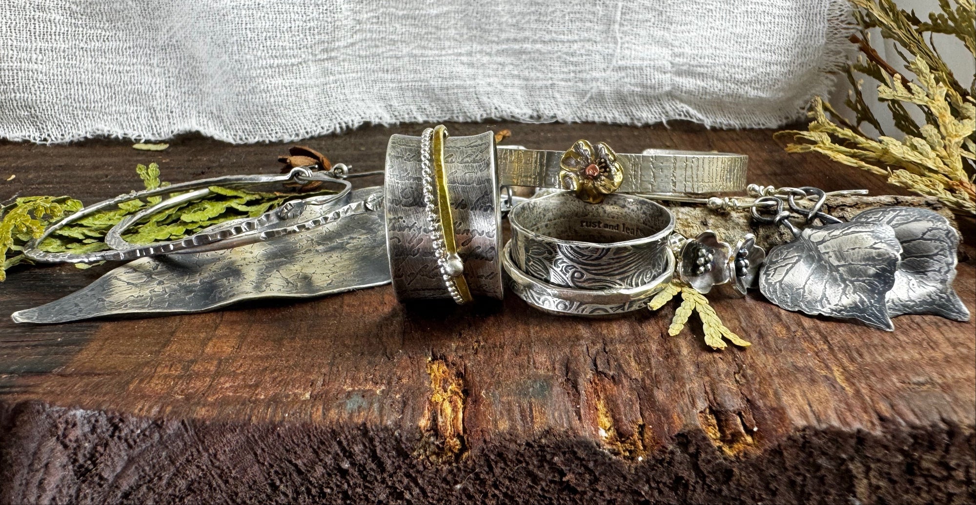 Collection of silver jewelry on a wooden surface with greenery