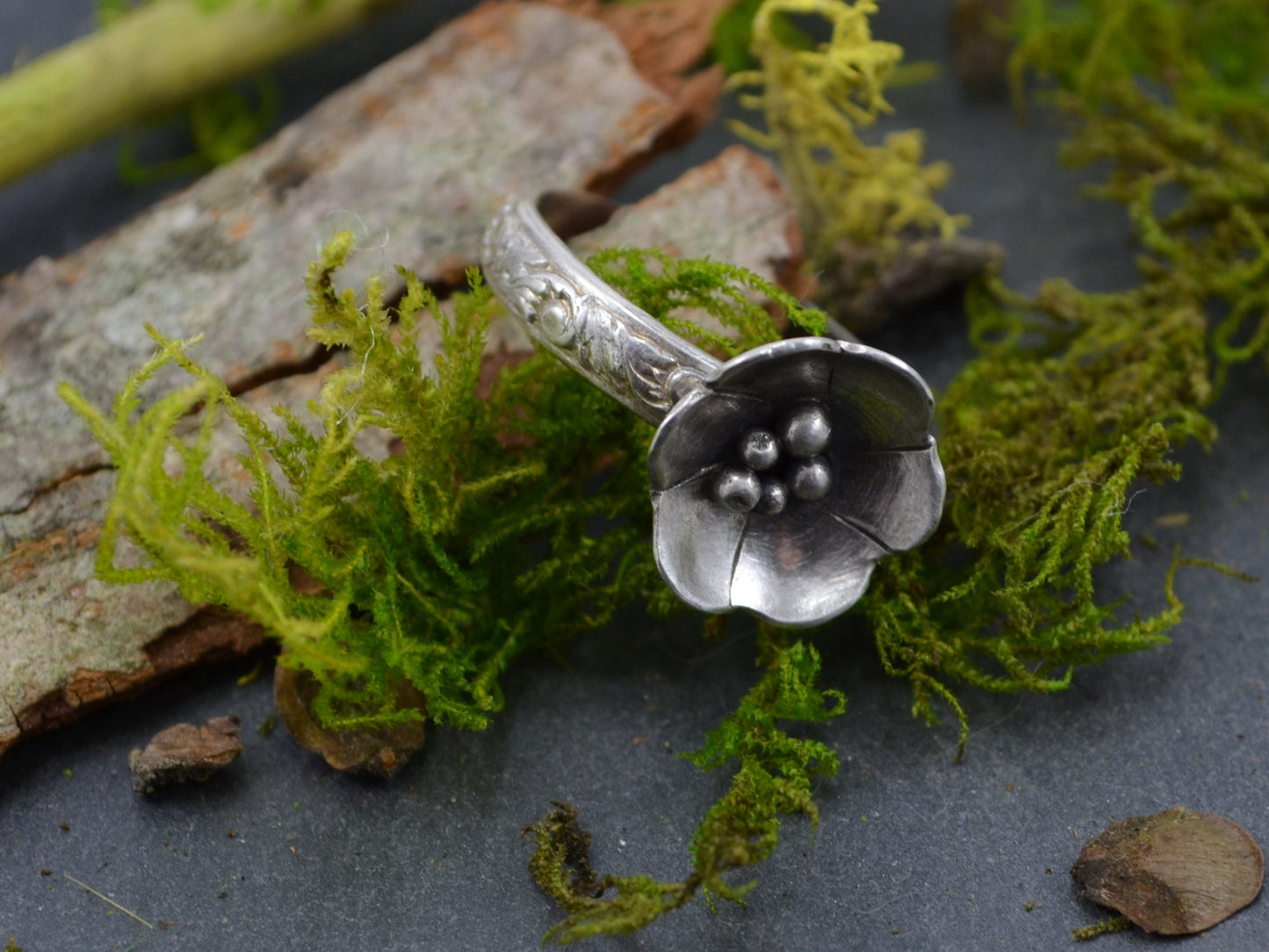 The Sterling Silver Deanna Flower Ring by Rust and Leaf displayed on a piece of tree bark with moss