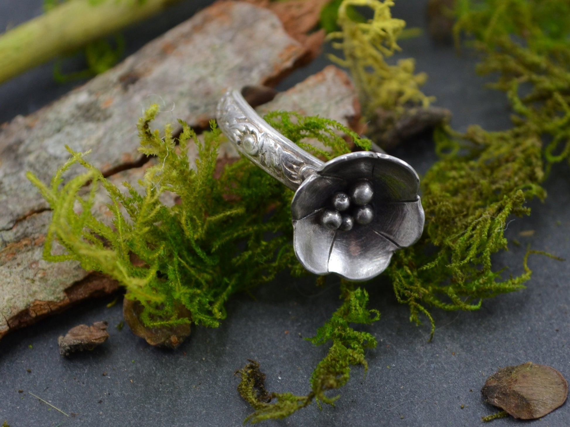 The Sterling Silver Deanna Flower Ring by Rust and Leaf displayed on a piece of tree bark with moss