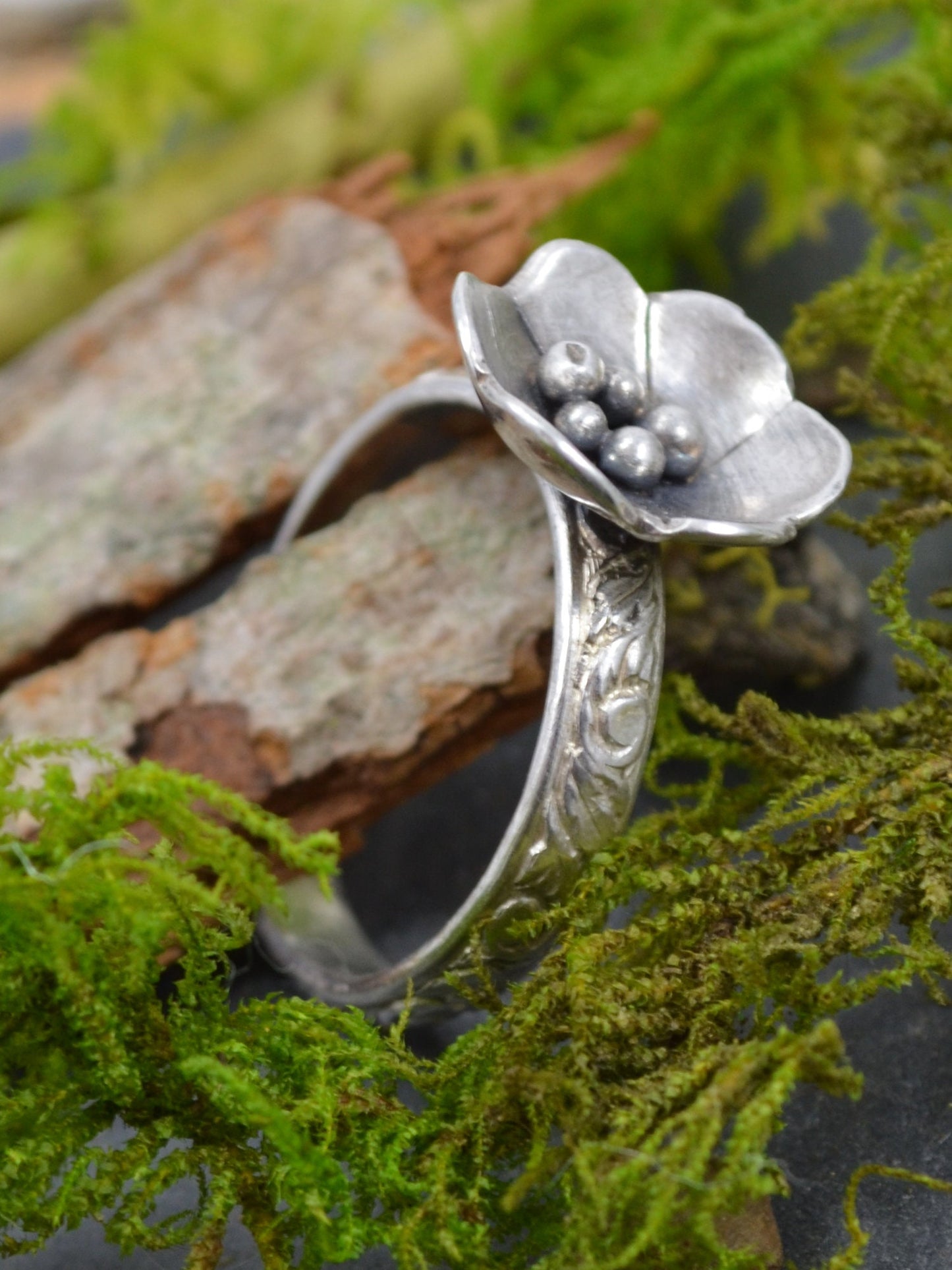 The Deanna Flower Ring by Rust and Leaf, displayed beautifully on a piece of tree bark nestled in green moss