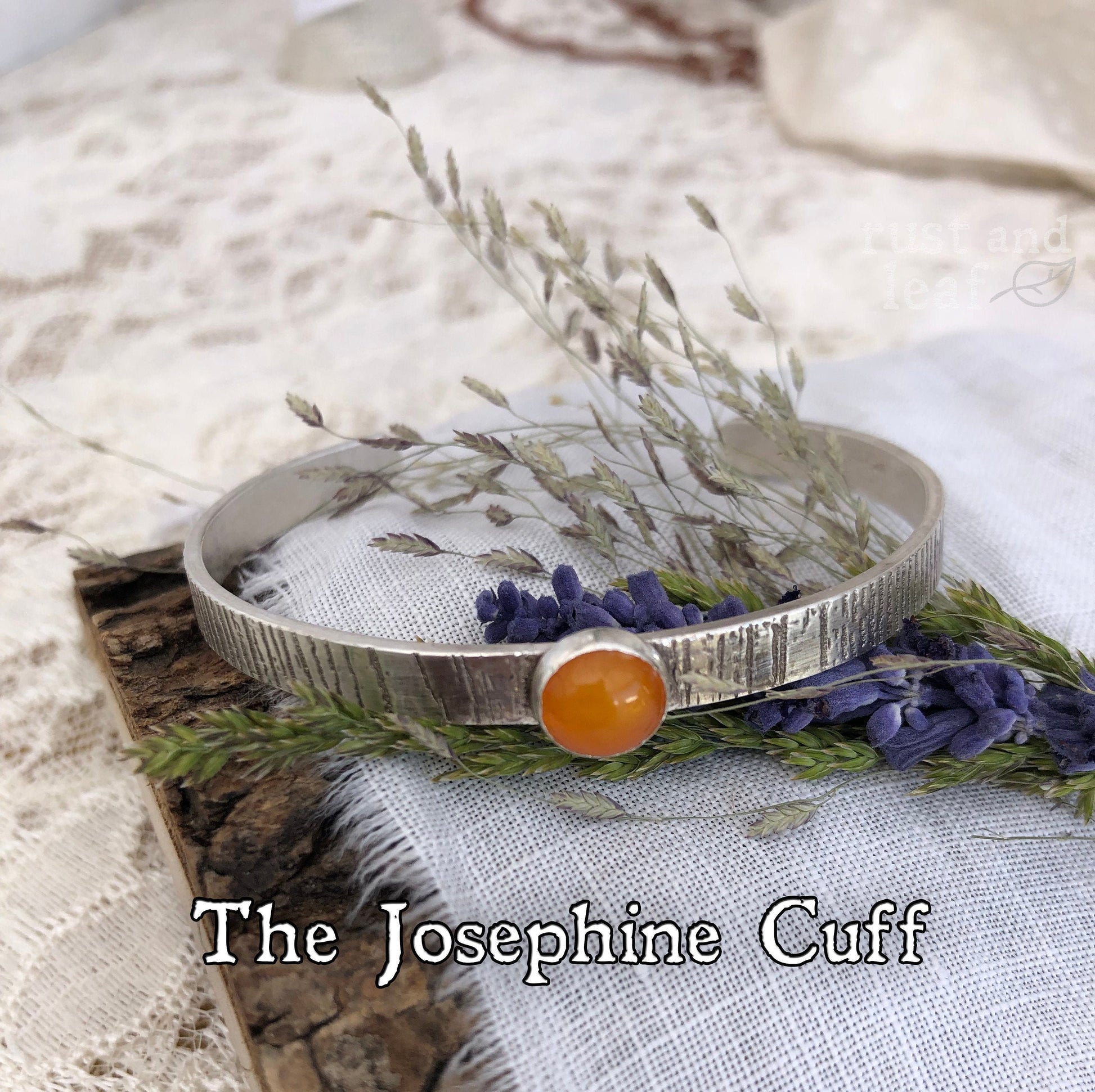 A rustic sterling silver cuff with bark-like texture and amber gem, resting on weathered wood, evoking ancestral forests.